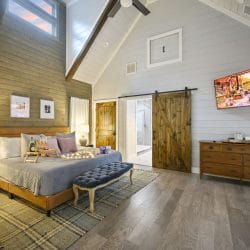 King bedroom with a wood-framed bed, a tufted bench, a barn door and a wall TV