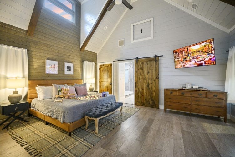 King bedroom with a wood-framed bed, a tufted bench, a barn door and a wall TV