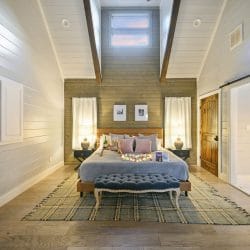 King bed under a wood accent wall with a tufted bench and plaid rug, the barn door open to the bath