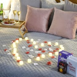Bed set with candles in a heart shape, rose petals, a breakfast tray and champagne flutes