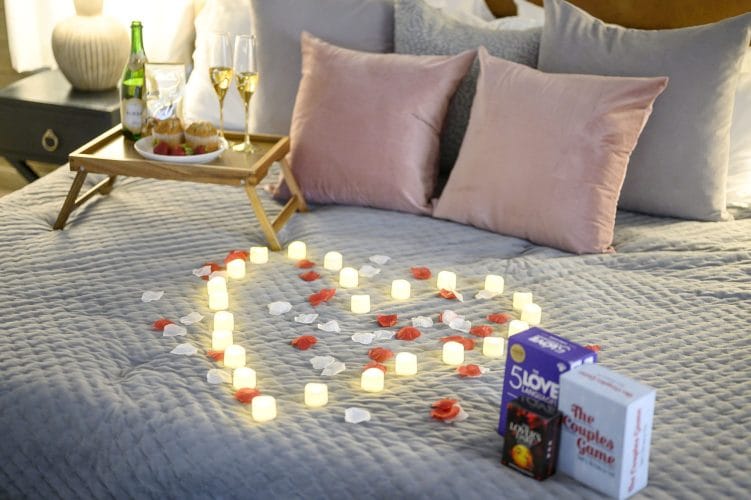 Bed set with candles in a heart shape, rose petals, a breakfast tray and champagne flutes