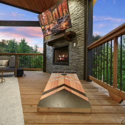 Covered deck with a fireplace, a lounge sofa and a cornhole board beside the railing