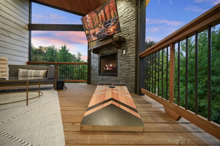 Covered deck with a fireplace, a lounge sofa and a cornhole board beside the railing