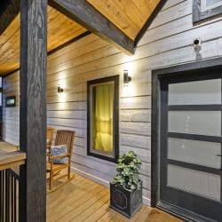 Front door under a porch roof with a rocking chair and a lit window