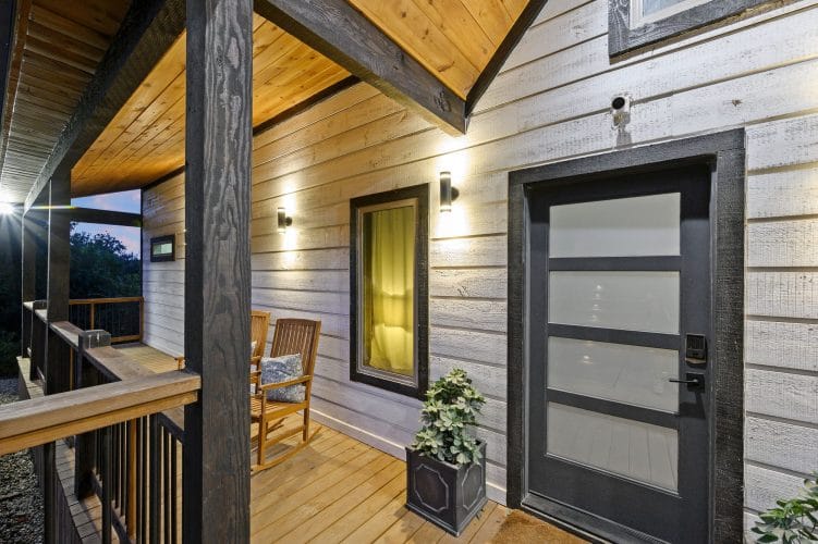 Front door under a porch roof with a rocking chair and a lit window