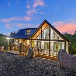 Front of the cabin with a tall glass gable, a deck and large boulders at dusk
