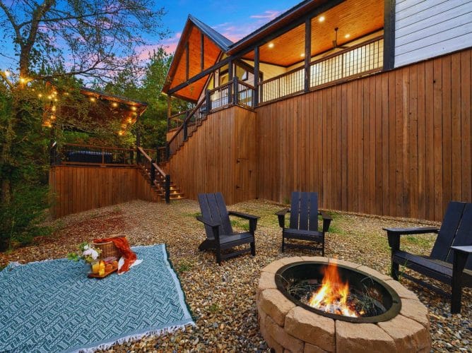 Fire pit with Adirondack chairs and a picnic spread, with the cabin siding behind