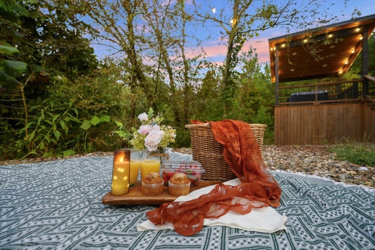 Picnic blanket with a basket and drinks on the gravel near the fire pit