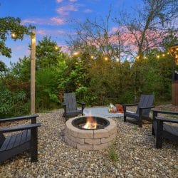 Fire pit with Adirondack chairs and string lights on gravel