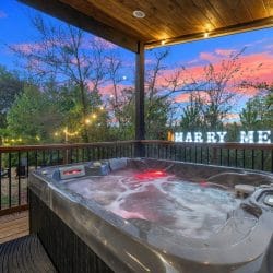 Hot tub on a covered platform at dusk, with a lit marquee sign on the rail