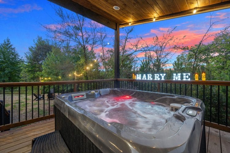 Hot tub on a covered platform at dusk, with a lit marquee sign on the rail