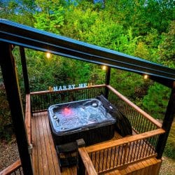 Hot tub on its own platform under a pergola roof, with string lights in the trees