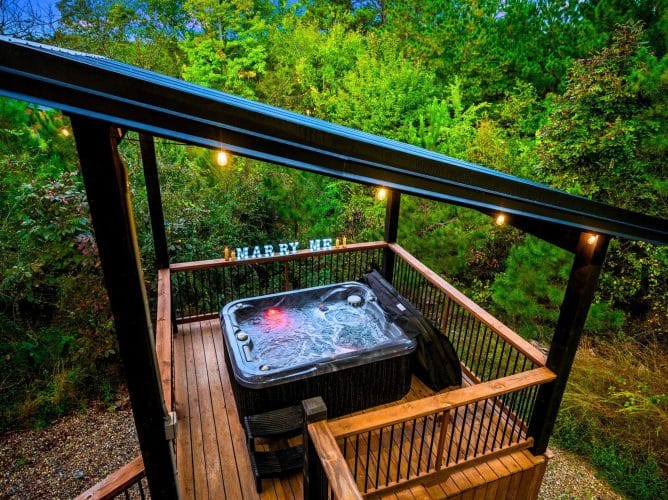 Hot tub on its own platform under a pergola roof, with string lights in the trees
