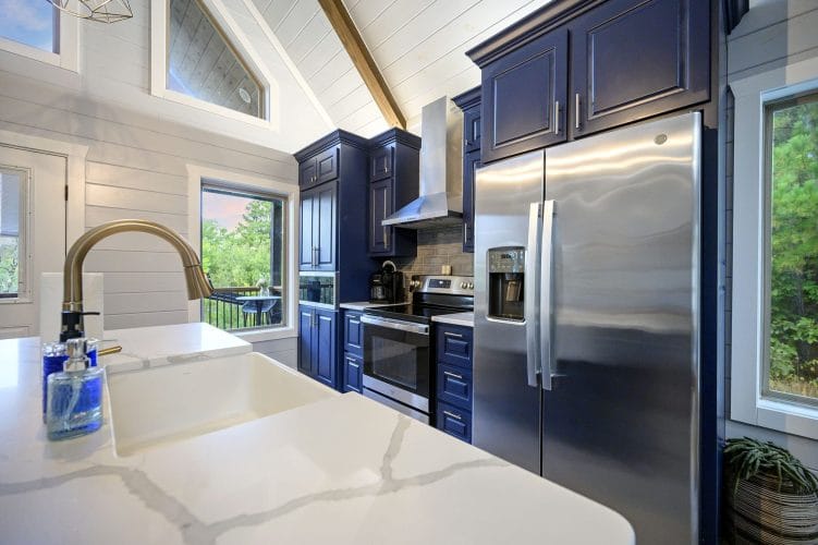 Farmhouse sink in a white quartz counter with a stainless refrigerator behind