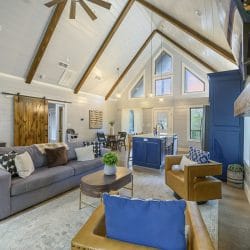 Living area with vaulted beams and a gray sofa, the navy kitchen island behind