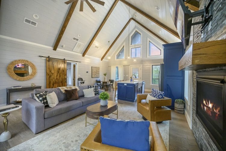 Living area with vaulted beams and a gray sofa, the navy kitchen island behind
