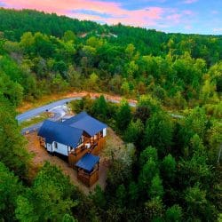 Aerial of the cabin with a blue roof in a green forested valley