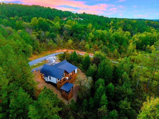 Aerial of the cabin with a blue roof in a green forested valley