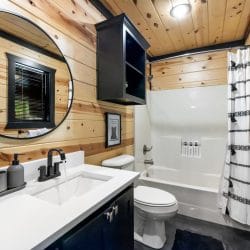 Bathroom with a white vanity, a round mirror, a toilet and a tub-shower with a striped curtain