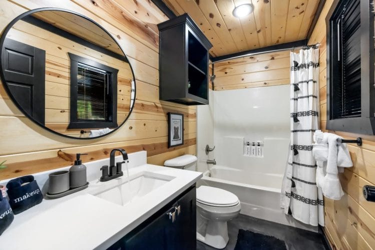 Bathroom with a white vanity, a round mirror, a toilet and a tub-shower with a striped curtain