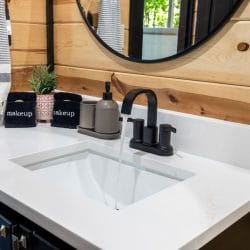 Close view of a white vanity with a black faucet and a round mirror