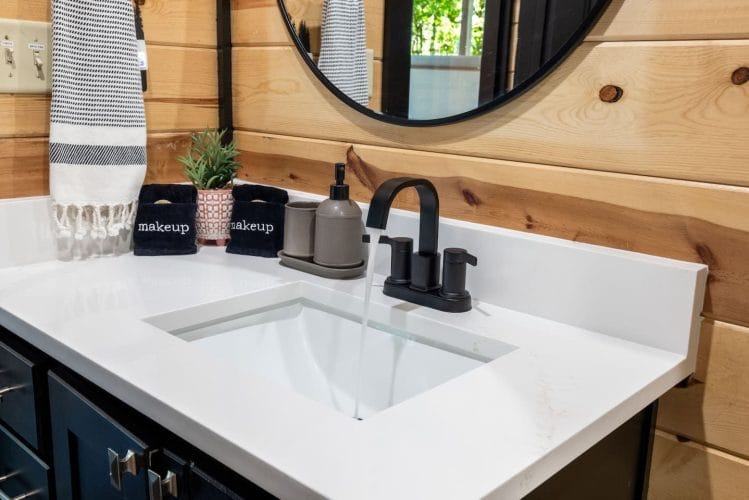 Close view of a white vanity with a black faucet and a round mirror