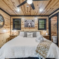 Bed with white linens, a bear photo and a round tree wall piece over the headboard, with a closet nook at right