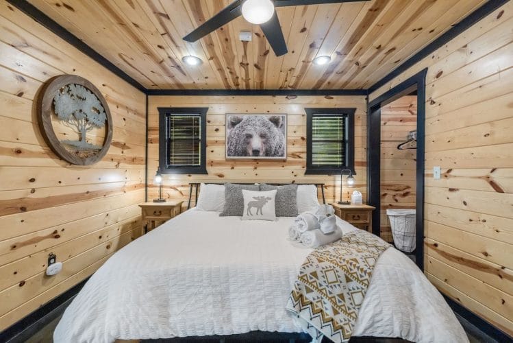 Bed with white linens, a bear photo and a round tree wall piece over the headboard, with a closet nook at right