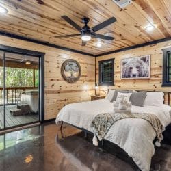 King bed with white linens and a throw, a bear picture above, and a sliding glass door to the porch