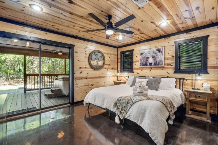 King bed with white linens and a throw, a bear picture above, and a sliding glass door to the porch