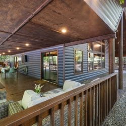 Covered porch running along the blue-gray siding with patio seating and glass doors to the house