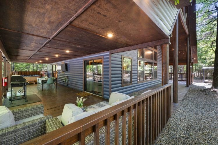 Covered porch running along the blue-gray siding with patio seating and glass doors to the house