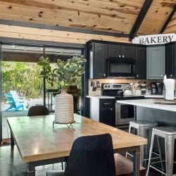 Wood dining table in front of an open glass door to the porch, with the kitchen island beside it