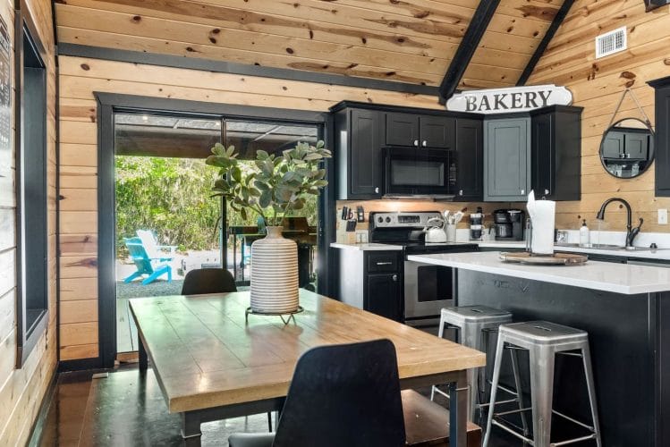 Wood dining table in front of an open glass door to the porch, with the kitchen island beside it