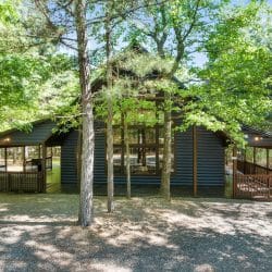 Side view of the cabin with the covered porch among trees and a gravel clearing