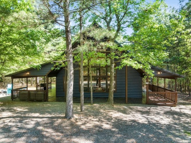 Side view of the cabin with the covered porch among trees and a gravel clearing