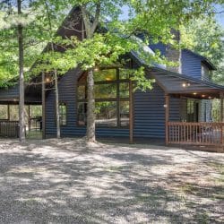 Cabin with a tall gable of windows, porch and gravel yard