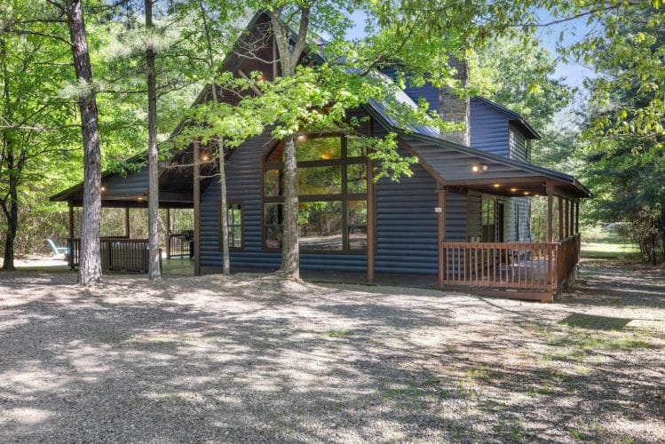 Cabin with a tall gable of windows, porch and gravel yard