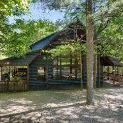 Wider view of the cabin and covered porch from the gravel drive