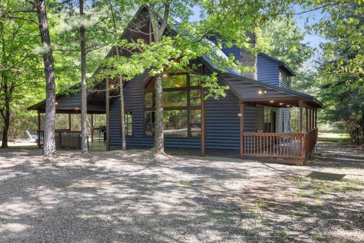 Cabin and gravel drive with leafy trees in the foreground