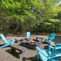 Fire pit in a gravel yard with turquoise Adirondack chairs and wooden benches around it