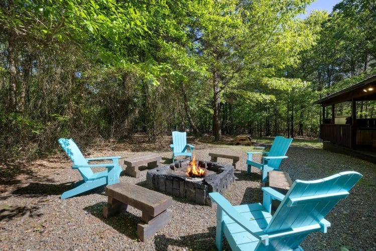 Fire pit in a gravel yard with turquoise Adirondack chairs and wooden benches around it