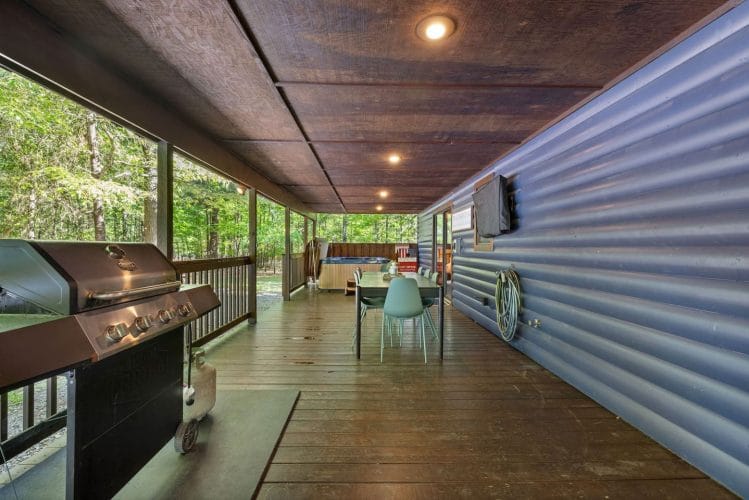 Gas grill on the covered porch with a long dining table and chairs beyond