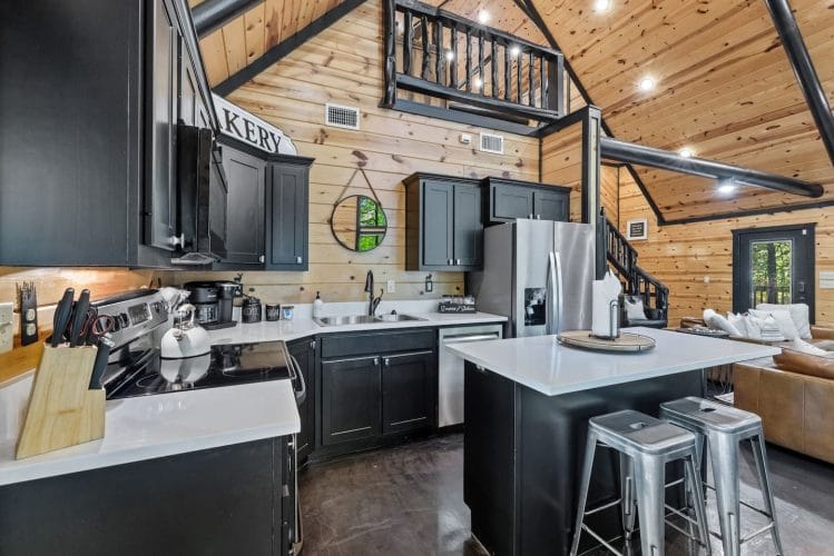 Kitchen with black cabinets, white counters, a stainless refrigerator and an island with metal stools