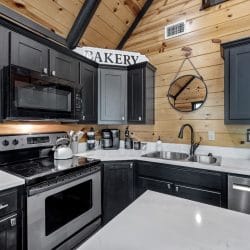 Corner of the kitchen with a stainless range, microwave and white counters under black cabinets