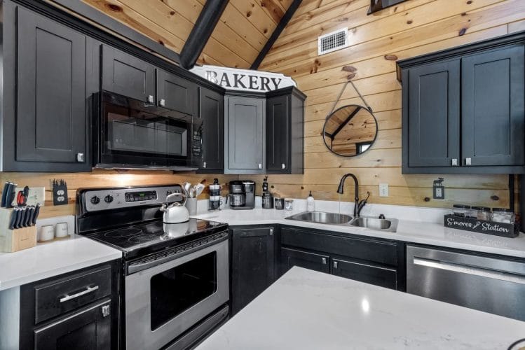 Corner of the kitchen with a stainless range, microwave and white counters under black cabinets