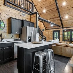 Island with metal stools and the living room beyond, under the loft railing
