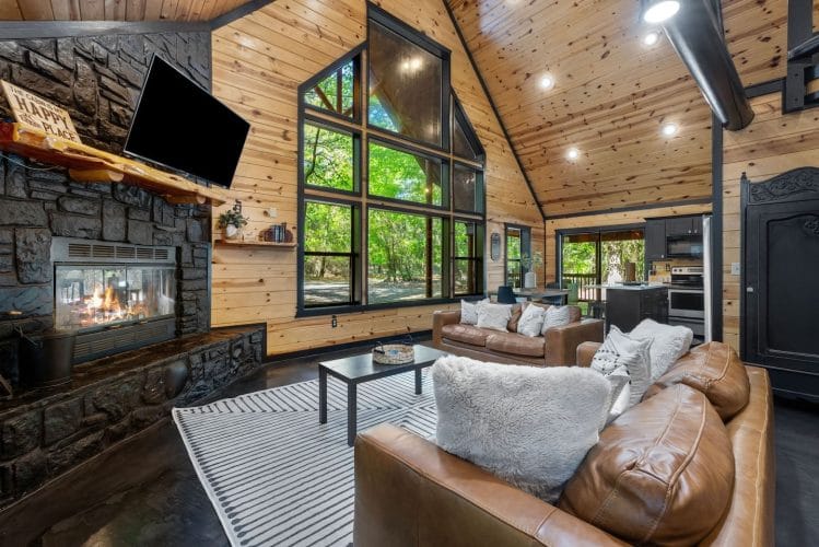Tall window wall beside the gas fireplace with a TV above it, looking out to the trees
