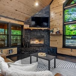 Gas fireplace burning, with windows on both sides and sofas with white pillows in front