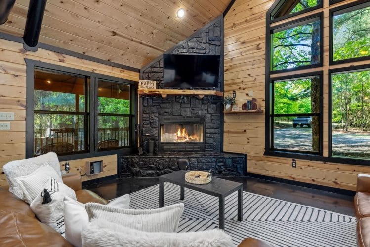 Gas fireplace burning, with windows on both sides and sofas with white pillows in front